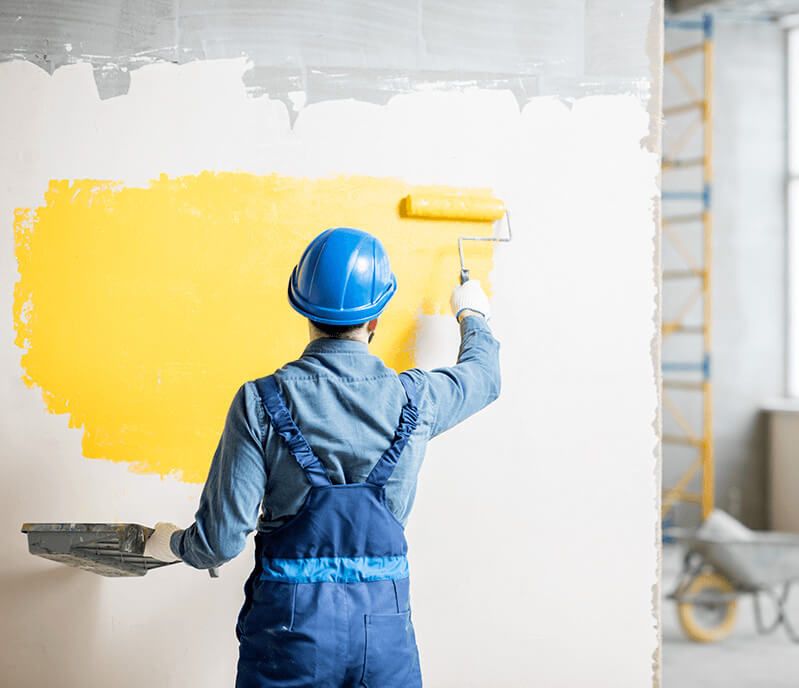 Man painting a white wall with yellow paint. 